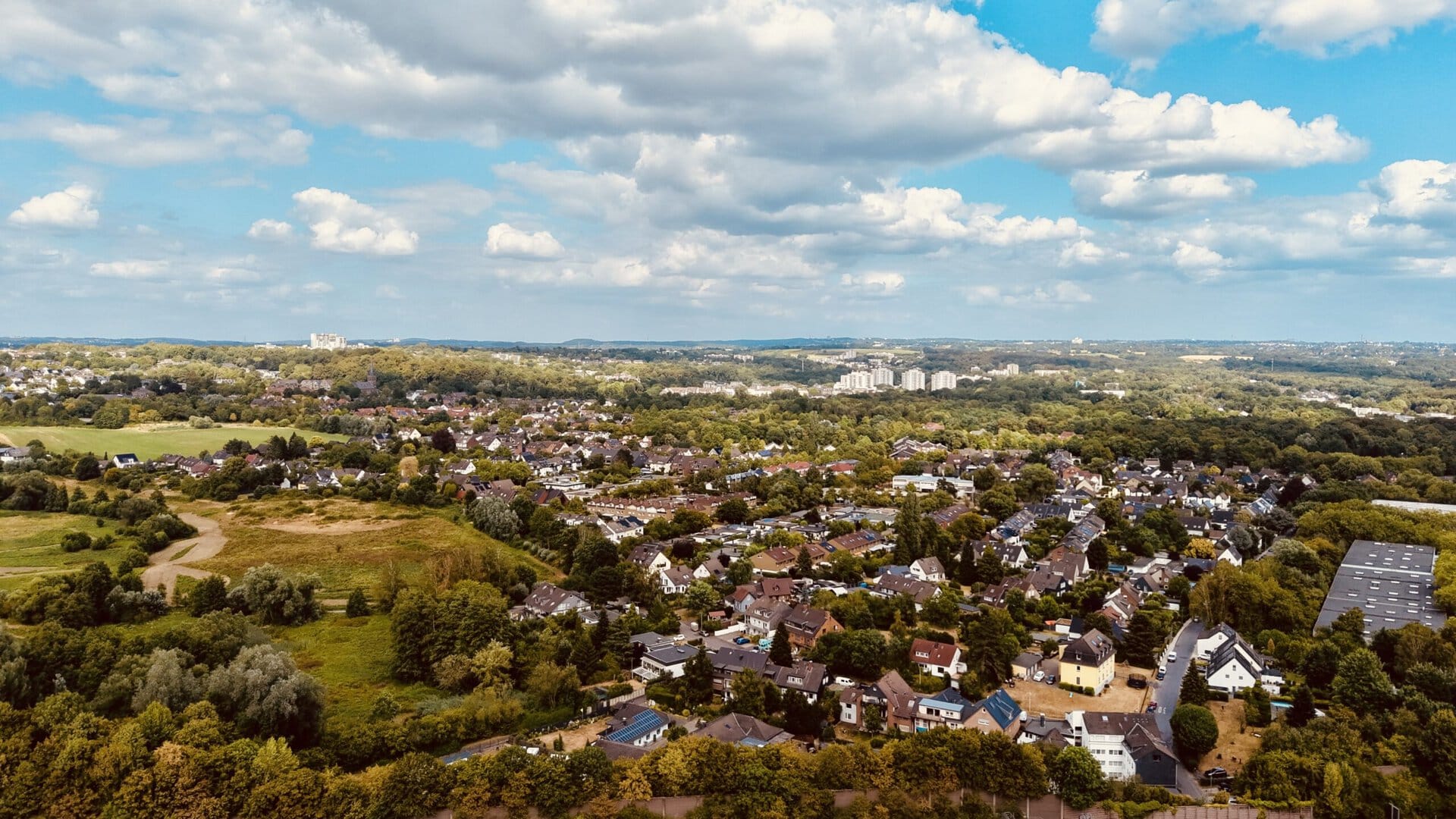 Luftaufnahme von Hochdahl mit grünen Feldern und Wohngebieten unter blauem Himmel.